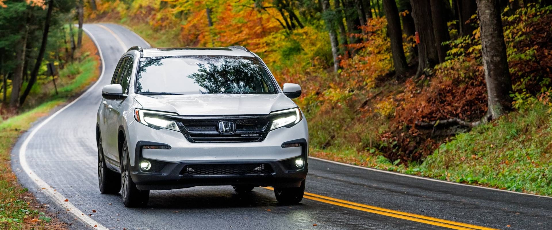White 2021 Honda Pilot driving on street with fall leaves on trees in background